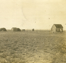 Historic photograph of a mostly empty landscape with a few structures in the distance