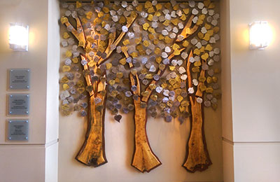 The sculpture features three stylized wooden trees with many metal leaves