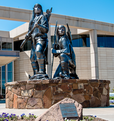 Bronze sculpture of two Apache warriors, one standing and one crouching, holding weapons