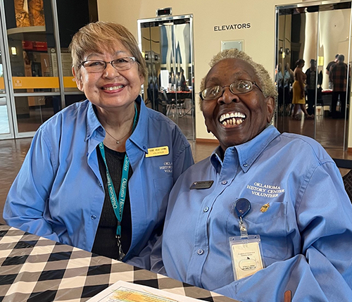 Two smiling volunteers seated at the Oklahoma History Center atrium