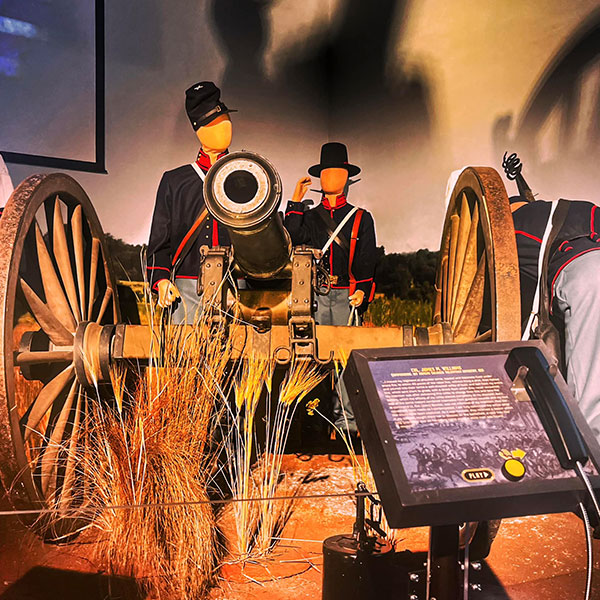 Male mannequins depicting two Union soldiers stand behind a large cannon. The brass cannon is atop a wooden gun carriage with two large wheels.