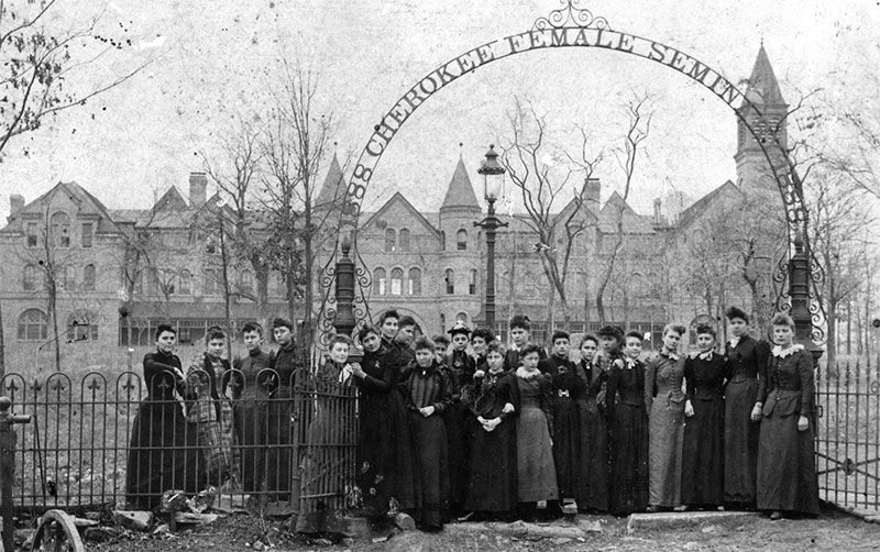 historic photo of a large group of women staning at the entrance gate to the grounds. The seminary is visible in the background.