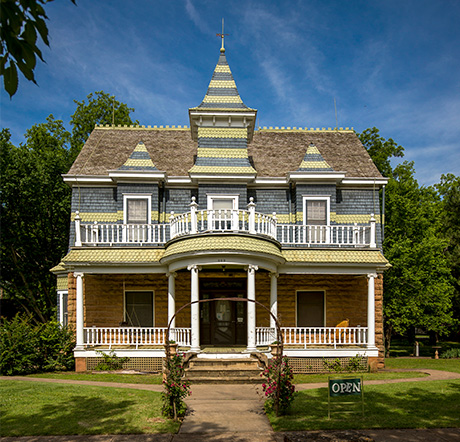 A three story Victorian Mansion with a circular second story balcony. Gingerbread style trim adorns the builing with a spire at the center, rising above the roofline.