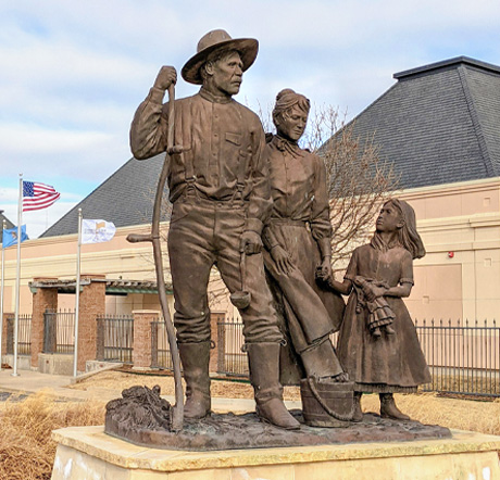 A statue of a pioneer man holding a scythe, a woman holding a hand of a female child.