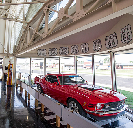 A two-door Mustang sportscar parked inside the large half oval bay of windows at the Oklahoma Route 66 Museum.