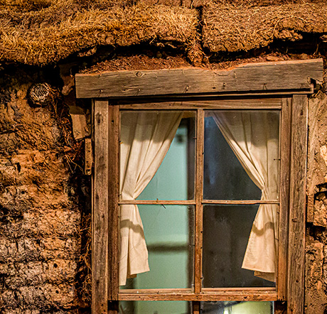 A crude wooden frame and window inserted into the sod bricks and roof of a sod home.