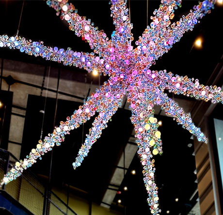 A contemporary sculpture with multiple starburst style arms, all lighted with small individual bulbs. The piece is entitled "The Power of Pop."