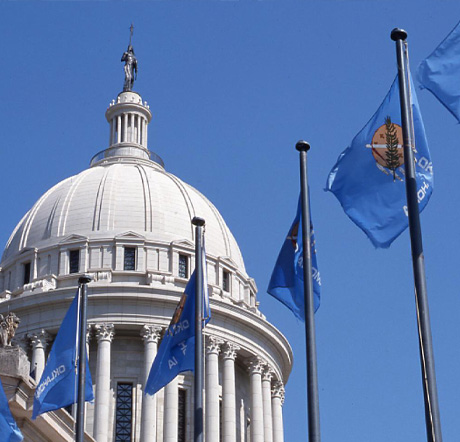 The dome and Windwalker statue of the Oklahoma State Capitol building. Several Oklahoma state flags are seen in the foreground.