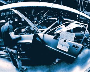 Three employees assemble a car at the Oklahoma City GM plant. The hood and doors of the car are open.