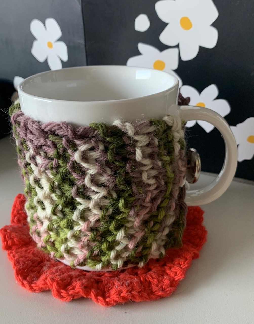 A mug with a multi-colored knitted cozy