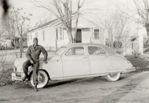 A soldier leaning against a parked car.