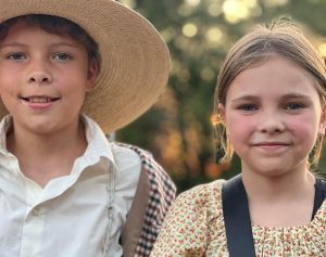 A boy and a girl in historic clothing smile at the camera.