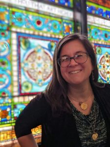 Megan McElfresh standing in front of a large bank of stained glass windows.