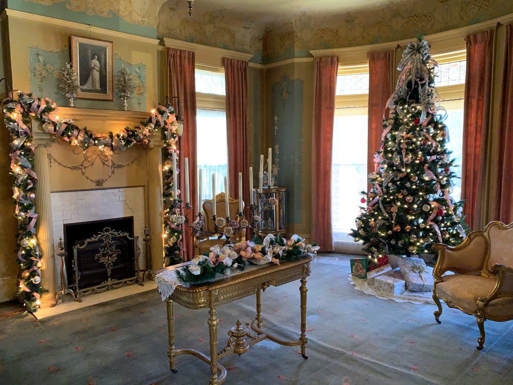 A Christmas tree, candles, and a fireplace garland decorate the parlor room at the Henry and Anna Overholser mansion.