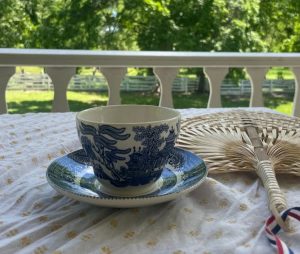 A tea cup with an Asian design and a hand-held fan on the porch at Hunters Home.