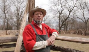 David Fowler Regional Director leans an elbow against the split rail fence he built at Hunters Home. Fowler is wearing farming clothes worn in the 1800s.