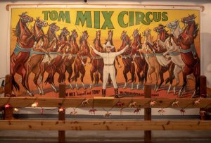 A mural display at the Tom Mix Museum with the words "Tom Mix Circus" and horses on their hind legs behind him