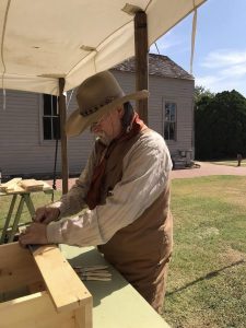 A living history actor, dressed in Western clothing works on a carpentry project outside the Enid Land Office at the Cherokee Strip Regional Heritage Center in Enid.