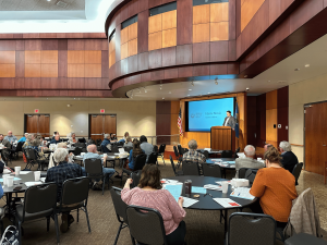 Trait Thompson stands in from of a podium, speaking to groups seated at tables in the Chesapeake Center for the Oklahoma History Symposium