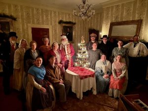 Living history actors dressed for the holiday gathered around a Christmas tree at the historic Hunters Home