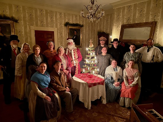 Living history actors dressed for the holiday gathered around a Christmas tree at the historic Hunters Home