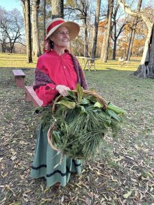 A woman in historic clothing holding a basketful of holiday greenery.
