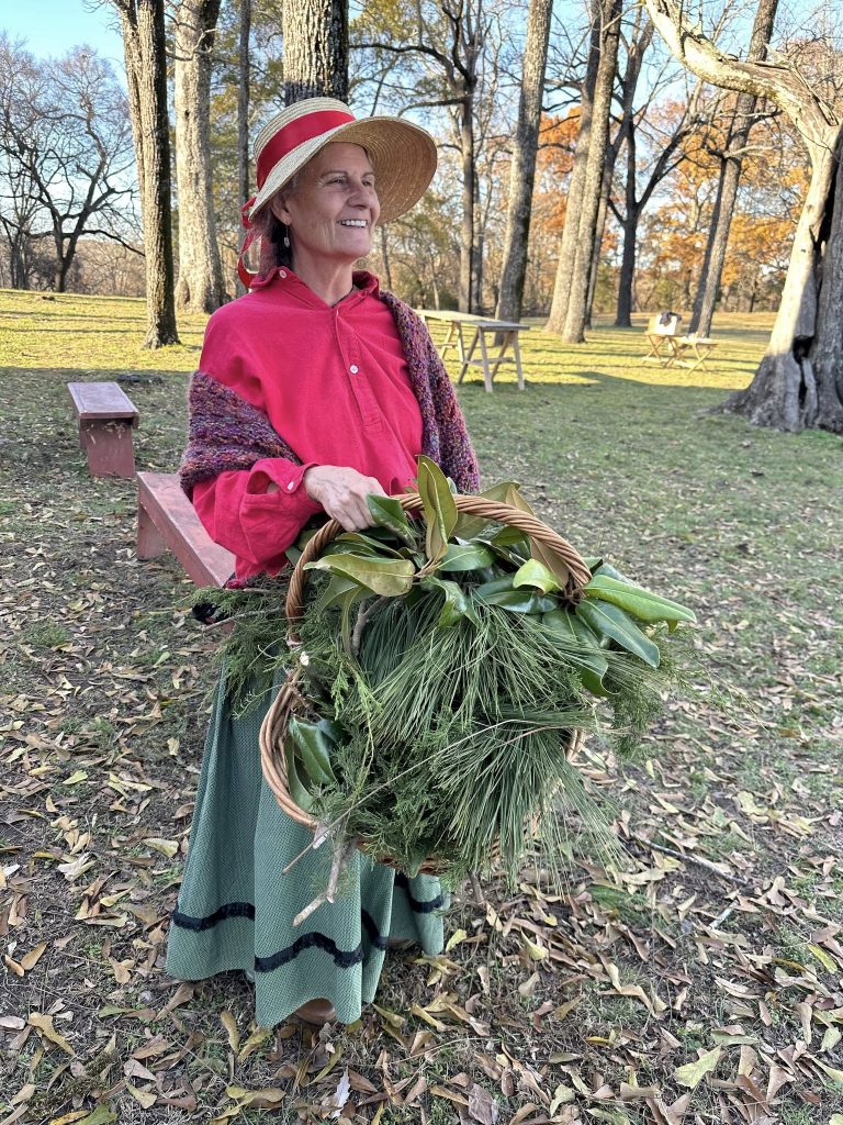 A woman in historic clothing holding a basketful of holiday greenery.