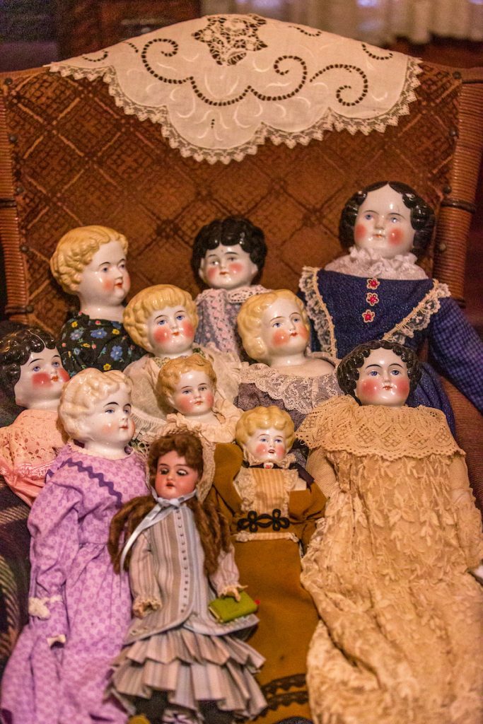 An antique chair with ten antique dolls grouped for display.
