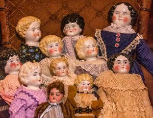An antique chair with ten antique dolls grouped for display.