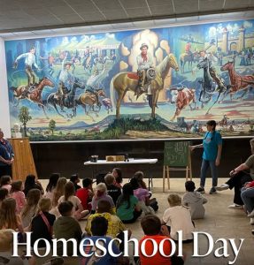 A Staff member teaching children at the Will Rogers Memorial Museum mural.