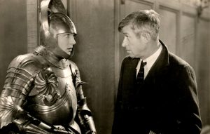 Will Rogers looks into the eye of Frank Alberston, who is wearing a suit of armor.