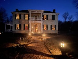 Lights of lanterns light the pathway to Hunter's Home. A starry sky overhead is the backdrop to the warm light in every window and door of the historic home.