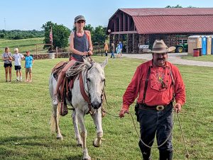 Kevin Webb dressed as Pawnee Bill leads his horse, with a child in the saddle.