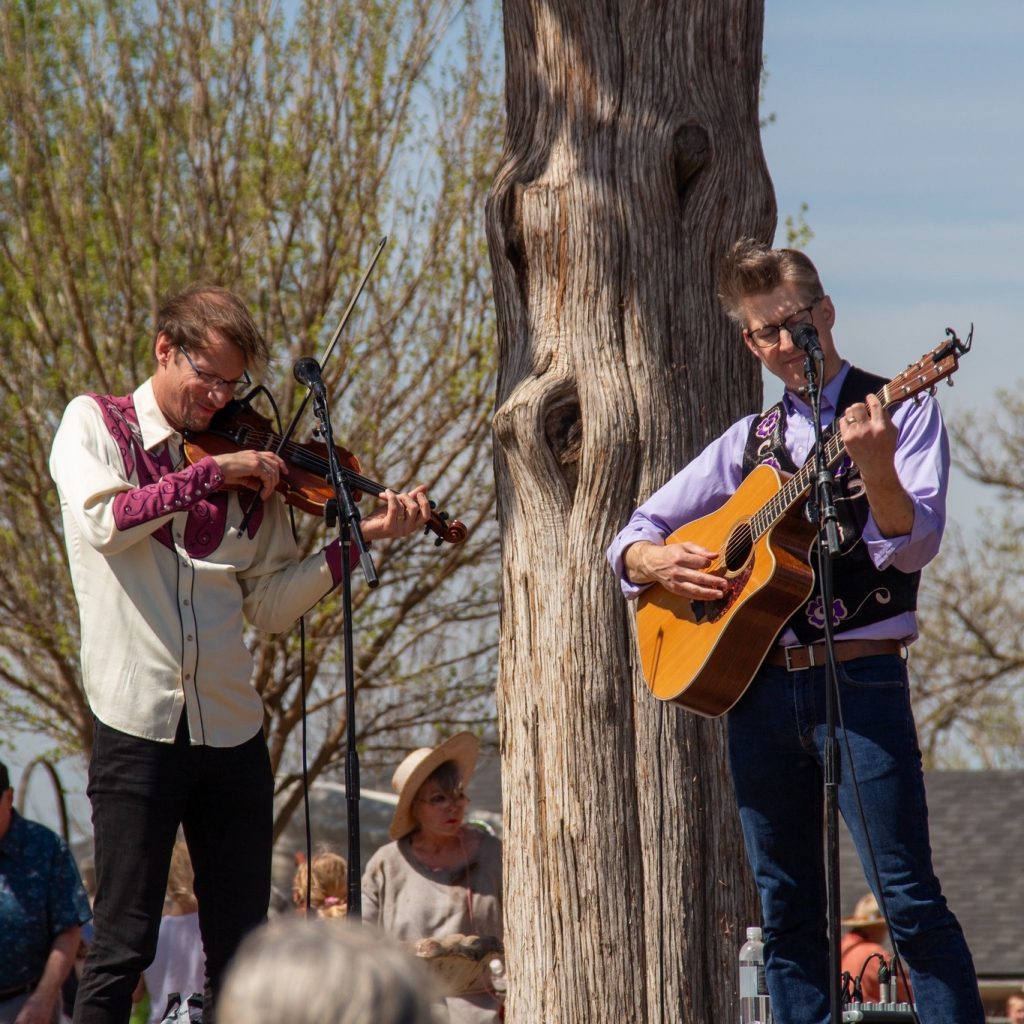 Two musicians playing fiddle and guitar at an outdoor gathering.