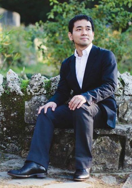 Ryoki Yamaguchi sitting on a stone seat in a public park.