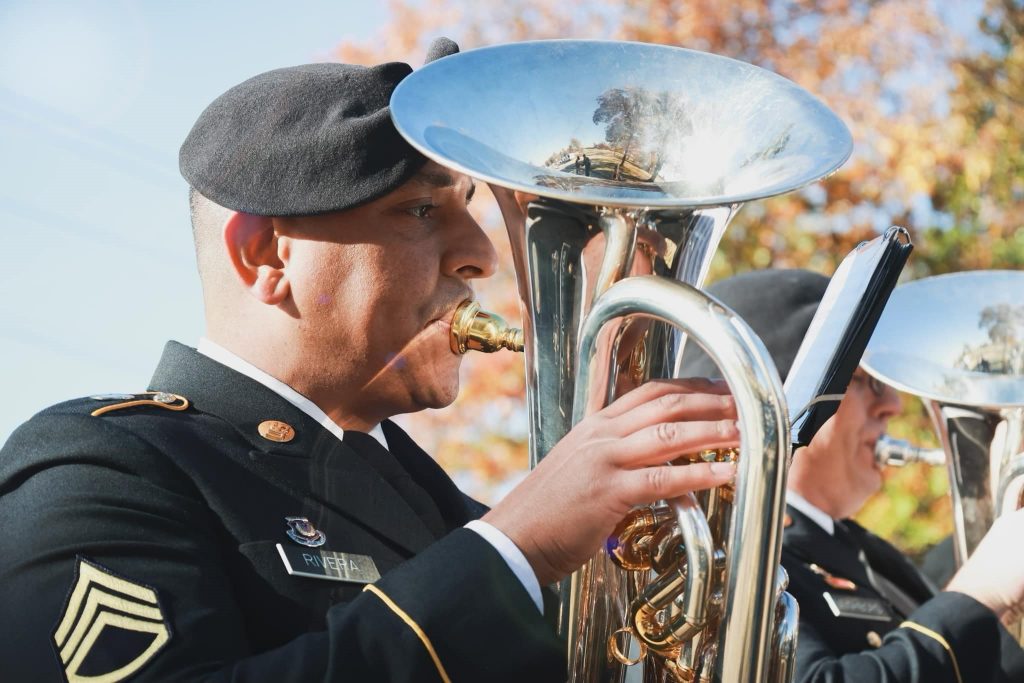An Army 395th band member plays a horned instrument in uniform.