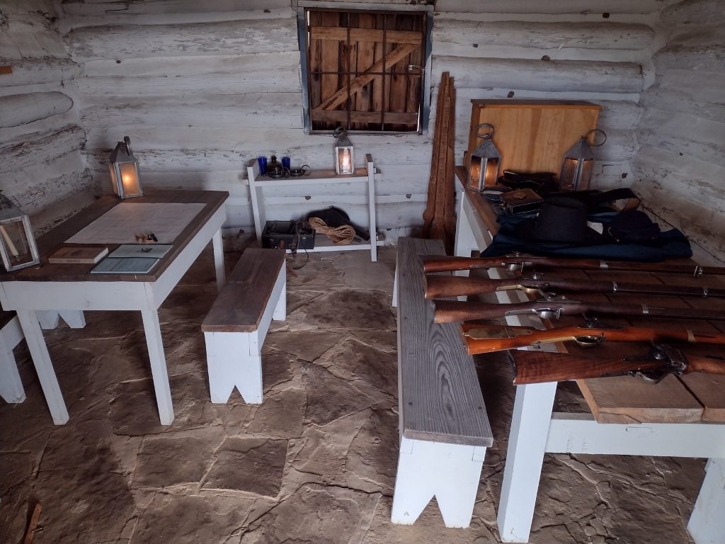 Long muskets, Union uniforms, lanterns are sitting on wooden tables in a room of the Fort Gibson stockade.