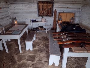 Long muskets, Union uniforms, lanterns are sitting on wooden tables in a room of the Fort Gibson stockade.