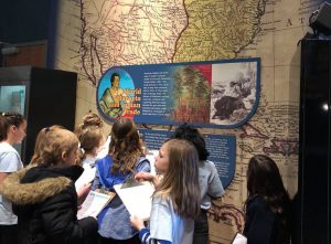 Children gather at an exhibit area with a map, imagery, and text on the wall.