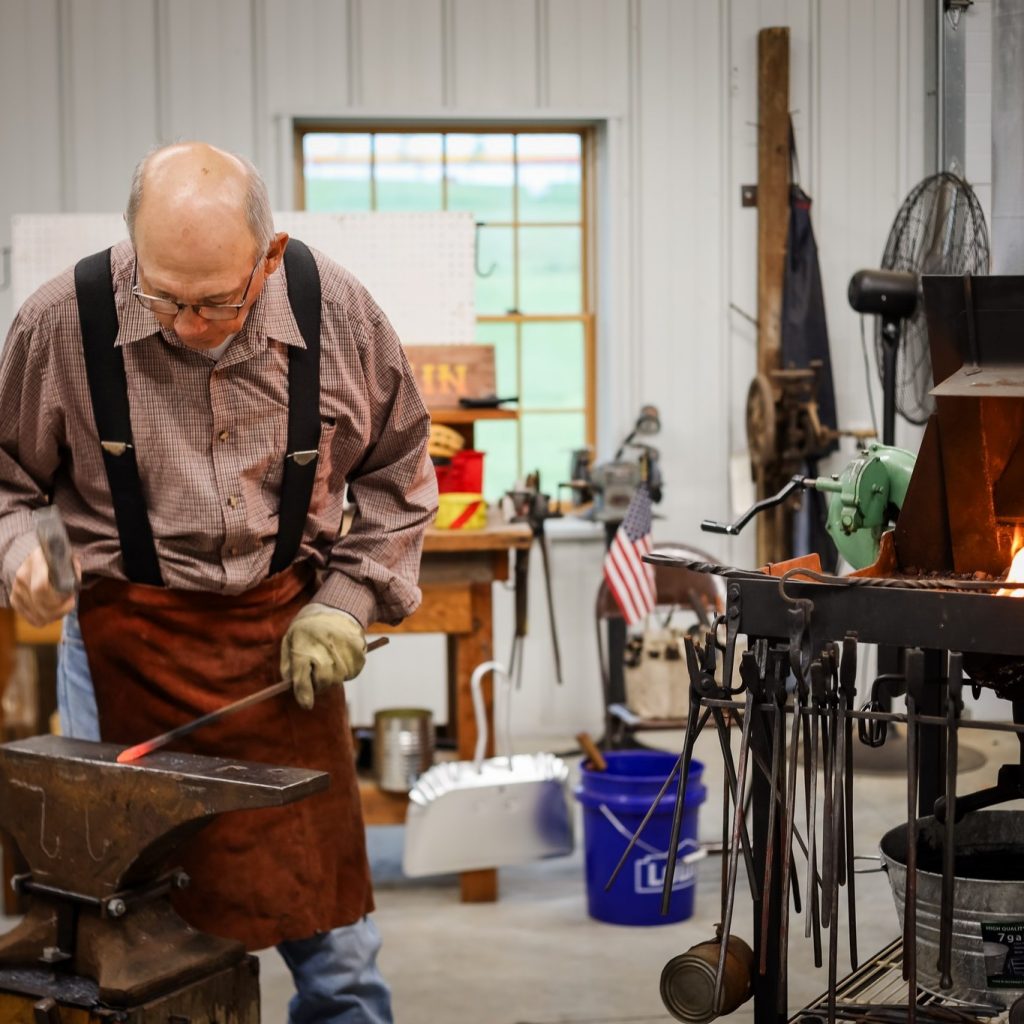 Tom Nelson, a blacksmith, works at the anvil with a red hot piece of iron.