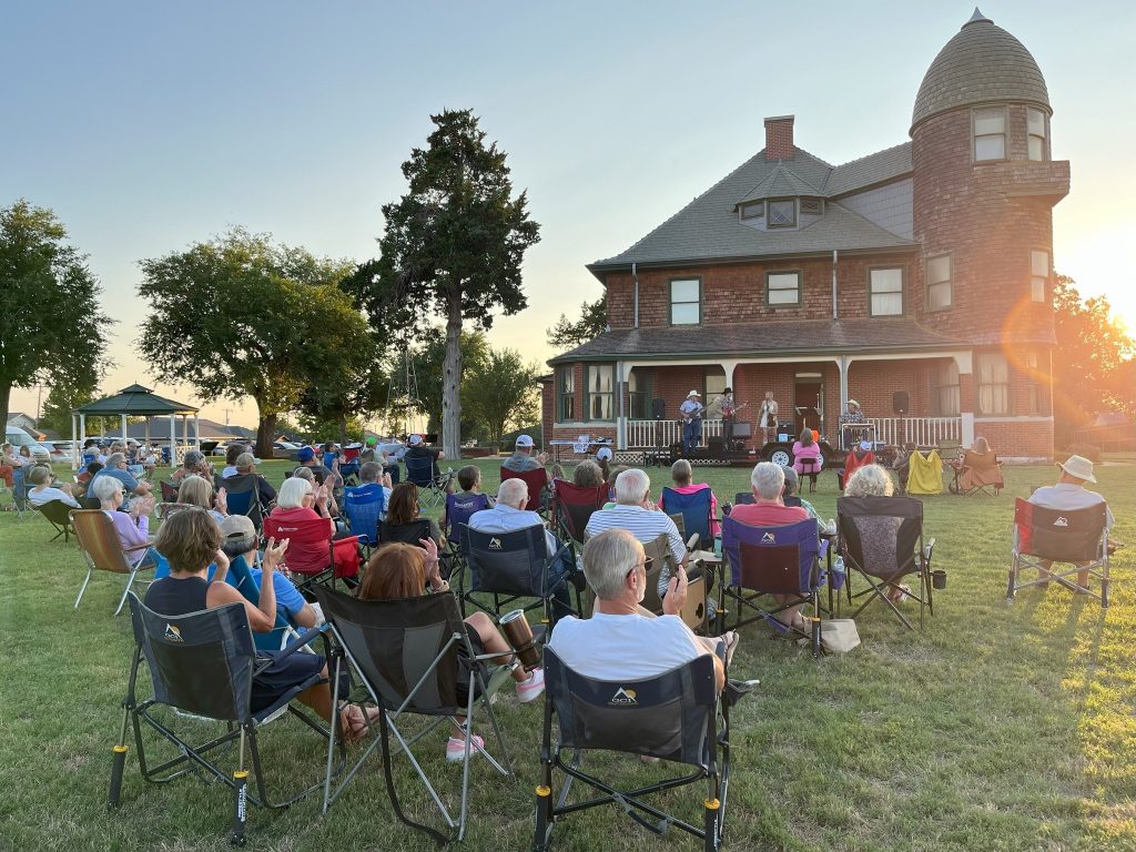 People seated in lawn chairs are entertained by live music at the Horizon Hill mansion in Kingfisher.