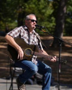 Singer Travis Kidd plays guitar, singing into a mic outdoors.