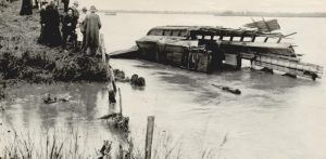 A passenger train in the Cimarron River with onlookers on shore