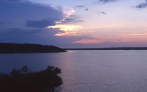 A scene on Kaw Lake at sunset, with trees growing on the edge of the body of water.