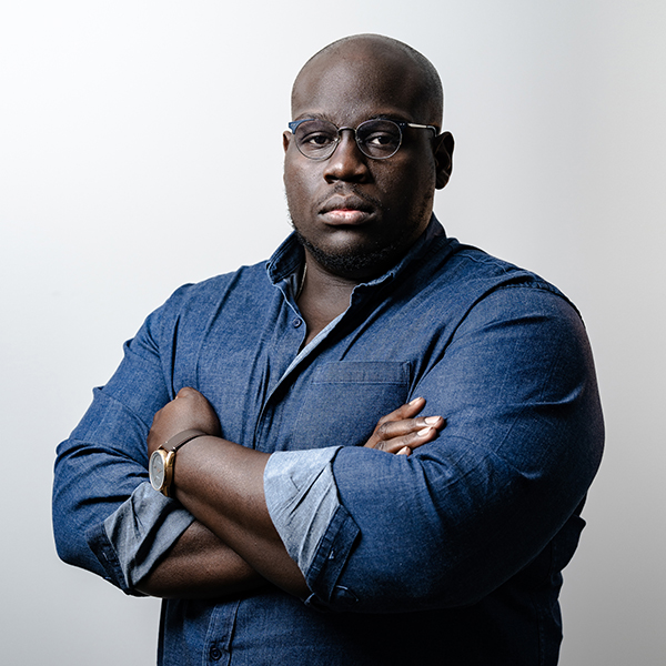 Caleb Gayle wearing a denim shirt with folded arms.
