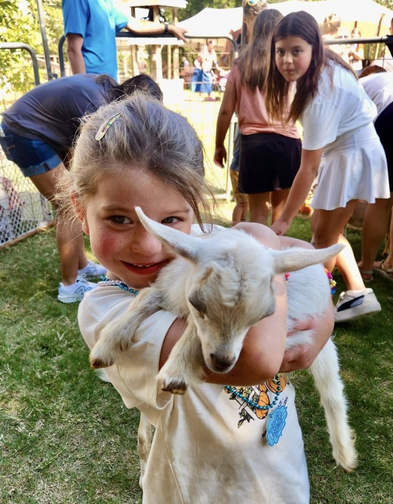 A young girl holds a baby goat in her arms.