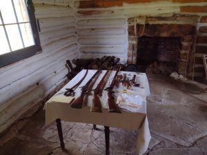 Muskets, pistols, and sabers laying on a table in a log-cabin style room at Fort Gibson.