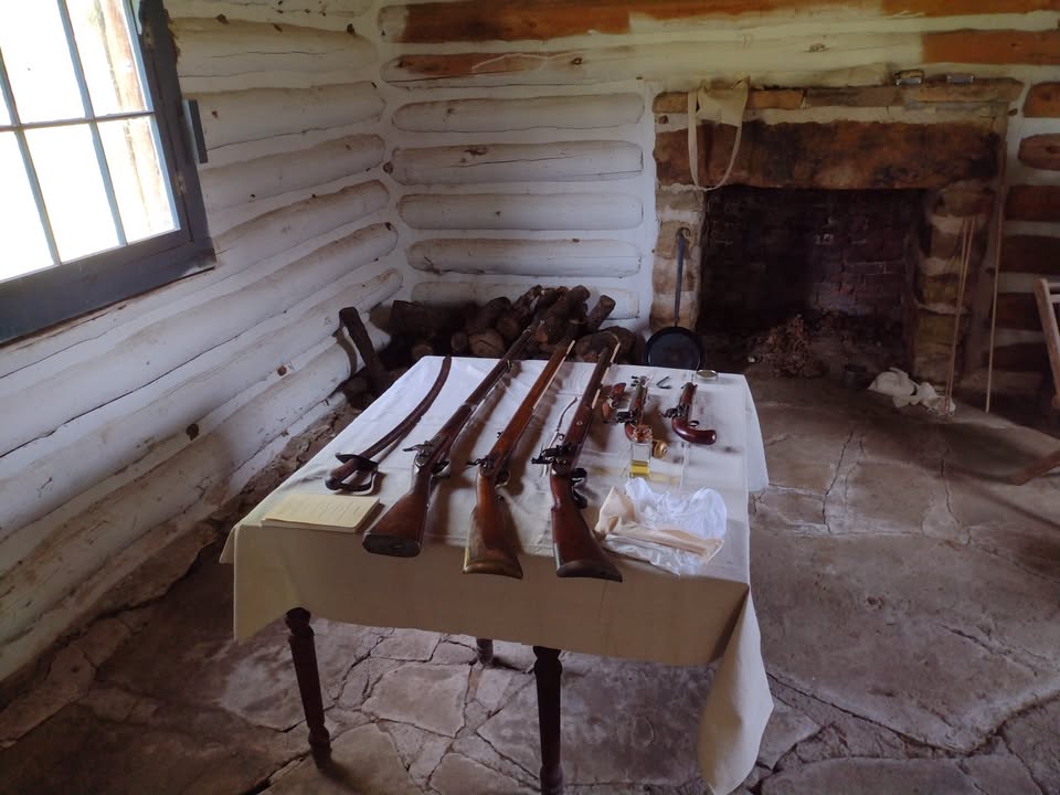 Muskets, pistols, and sabers laying on a table in a log-cabin style room at Fort Gibson.