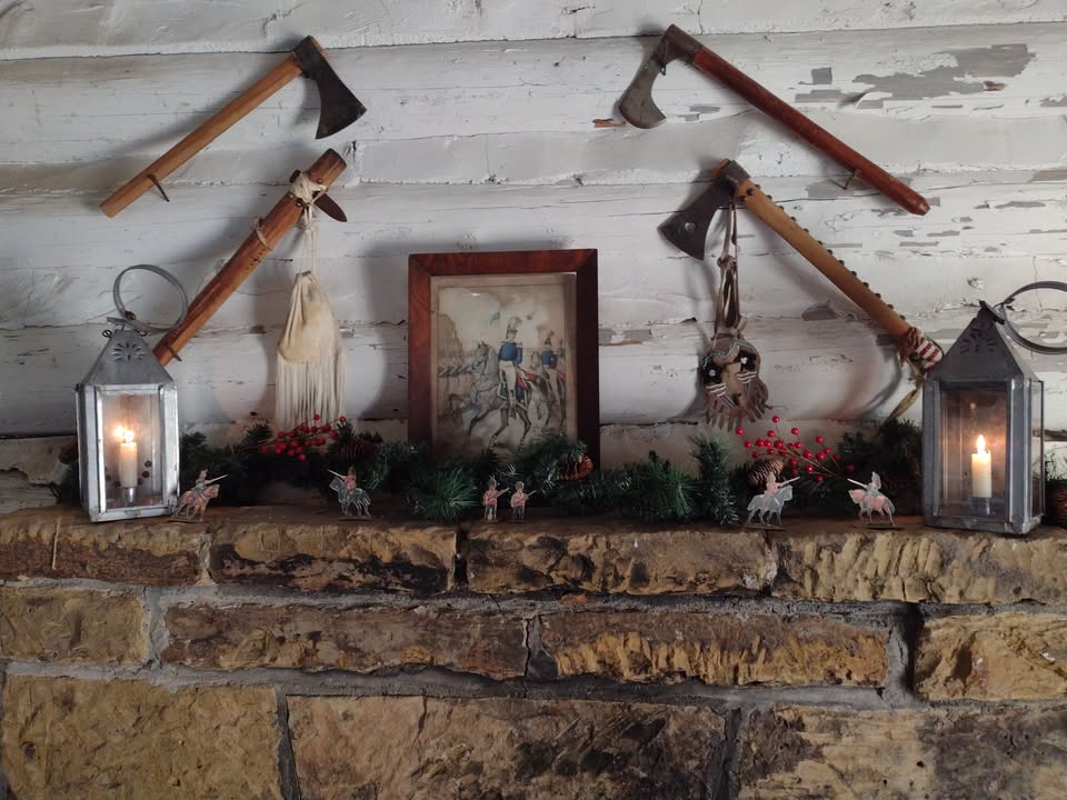 A framed picture, lit lanterns, and toy soldiers decorate a mantel in the soldier's palisade room. Hatchets adorn the wall above the fireplace.