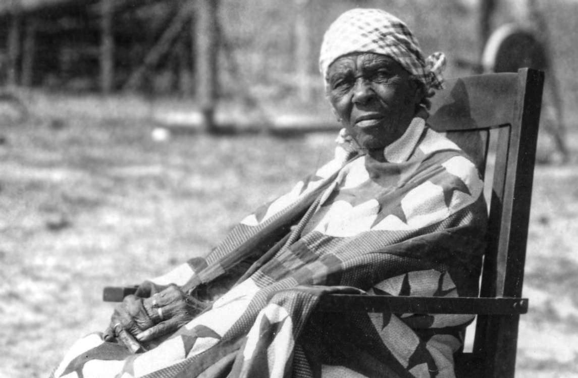 An elderly Freedman woman sits in a rocking chair outside